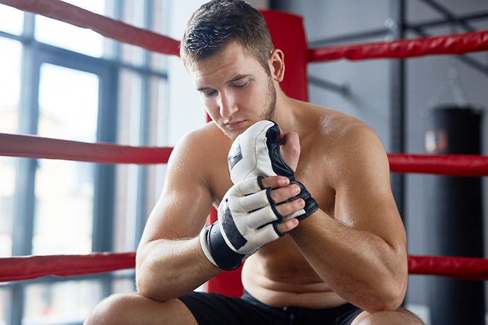 casl-ring Jeune pratiquant de MMA à Avignon appuyé sur les cordes d’un ring, portant des gants d’entraînement et concentré avant une séance de sports de combat.