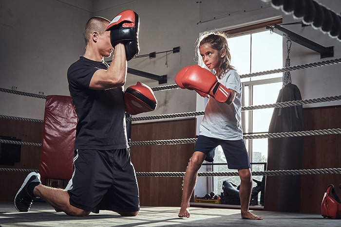 Enfant pratiquant un entraînement de kickboxing à Avignon avec un coach dans un ring de boxe, équipé de gants de protection rouges.